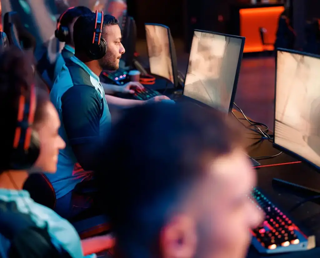 Kilku graczy gra razem przy komputerach w klubie e-sportowym. Gracze noszą słuchawki i komunikują się, biorąc udział w meczu.
