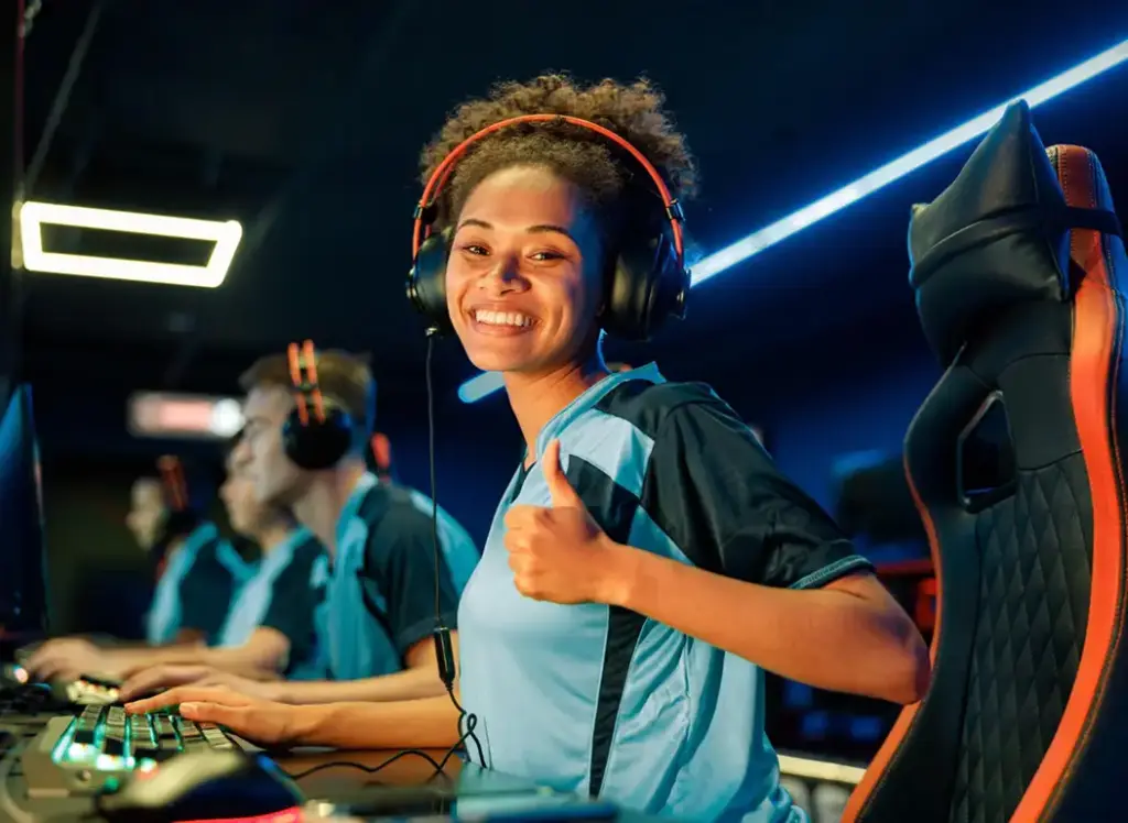 Kobieta gracz e-sportowy nosi słuchawki i uśmiecha się, siedząc przy swoim komputerze do gier. Atmosfera w pokoju do gier jest kolorowa i pełna energii.