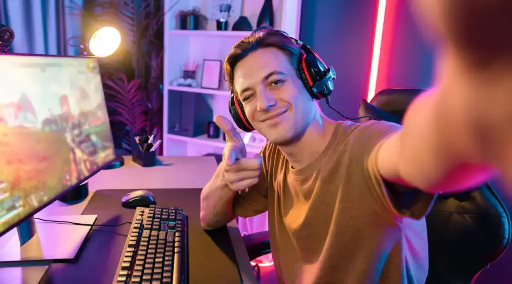 Gracz ze słuchawkami robi selfie przy swoim komputerze do gier. Siedzi w kolorowym pokoju do gier z neonowym oświetleniem.